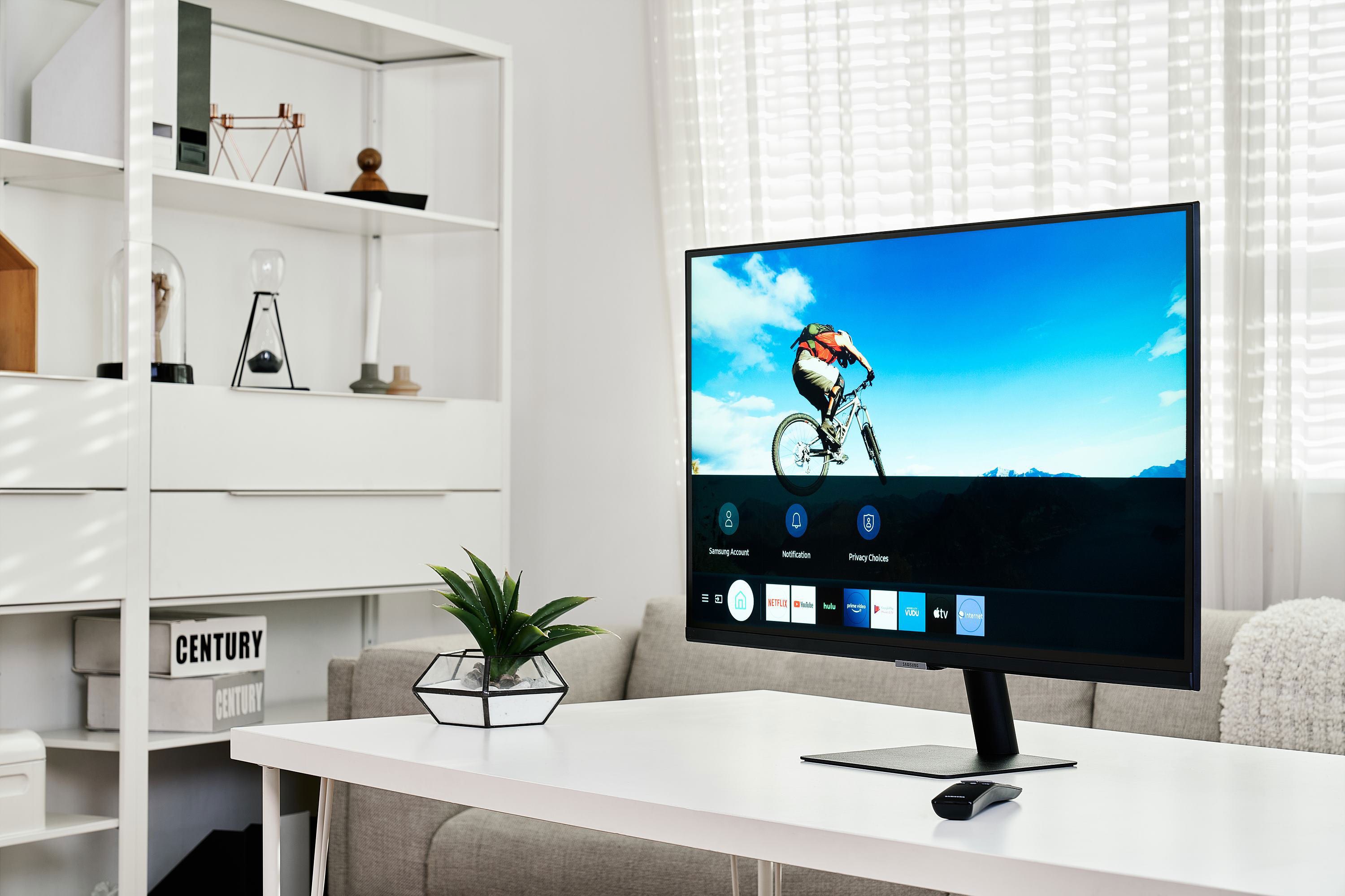 سامسونگ اسمارت مانیتور / Smart Monitor روی میز سفید داخل اتاق درحال نمایش آسمان آبی و دوچرخه